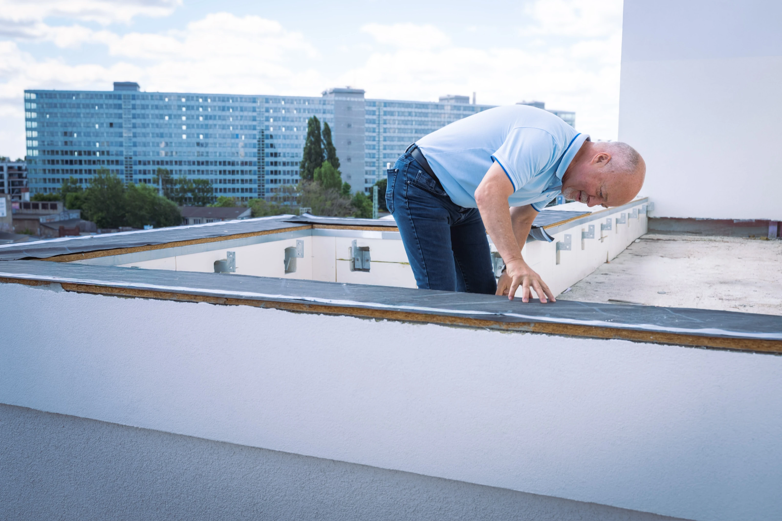 Ralf Händel beugt sich über einen Dachrand und betrachtet den Bauteilanschluss.
